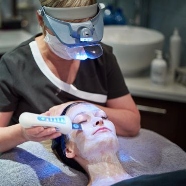 A skincare professional performs a facial treatment using a light therapy device.