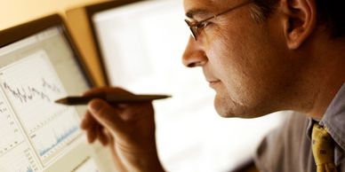 Man analyzing financial data on computer screens with a pen.