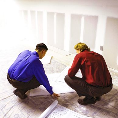 Two men in dress shirts reviewing architectural plans on a construction site.