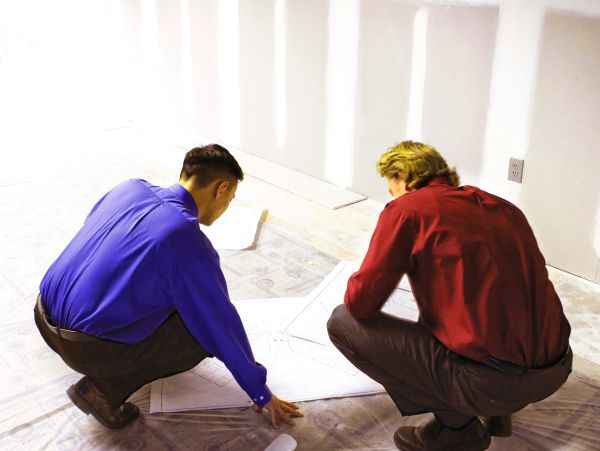 Two men in colorful shirts examining blueprints on the floor.