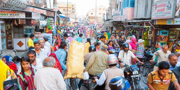 Crowded street market with people, bicycles, and motorcycles in an Indian city.