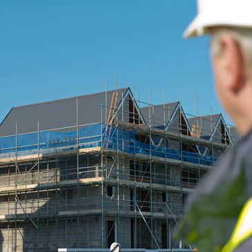 Construction worker observing a building under construction with scaffolding.