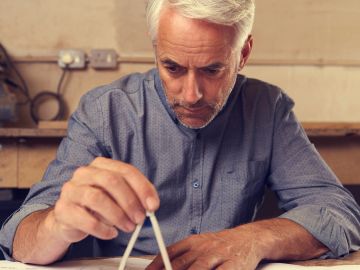 An elderly man carefully uses a compass for drawing or measuring.