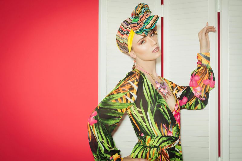 Exotic colorful fashion style with Caucasian model over red background. Silk long hippie dress and turban.