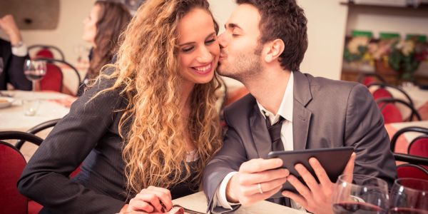 Couple sharing a kiss while using a tablet in a restaurant.