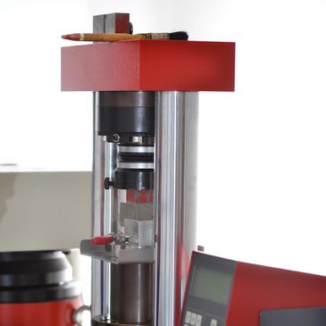 Concrete compression testing machine with a paintbrush and pencil on top.