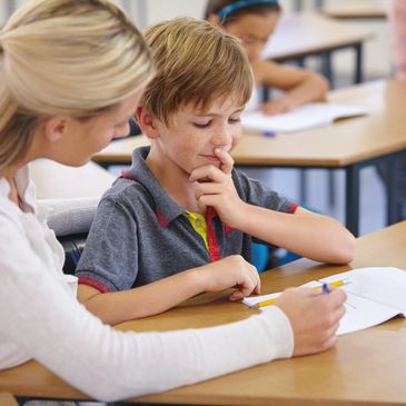 Teacher helping young boy with schoolwork at desk.