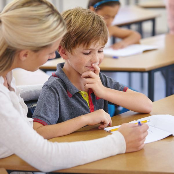 Teacher helping a young boy with schoolwork at a desk.