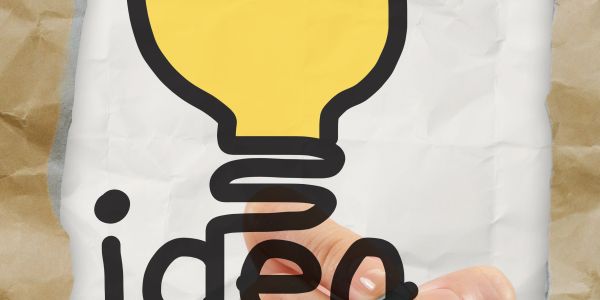 Hand pointing at a light bulb illustration labeled 'idea' on crumpled paper.