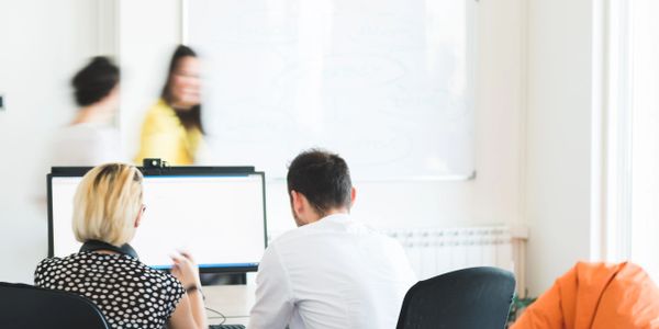 Two colleagues working together at a computer in a bright office.
