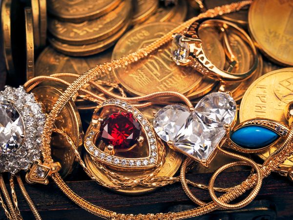 Close-up of a pile of gold coins with various gold and gem-encrusted jewelry on top.