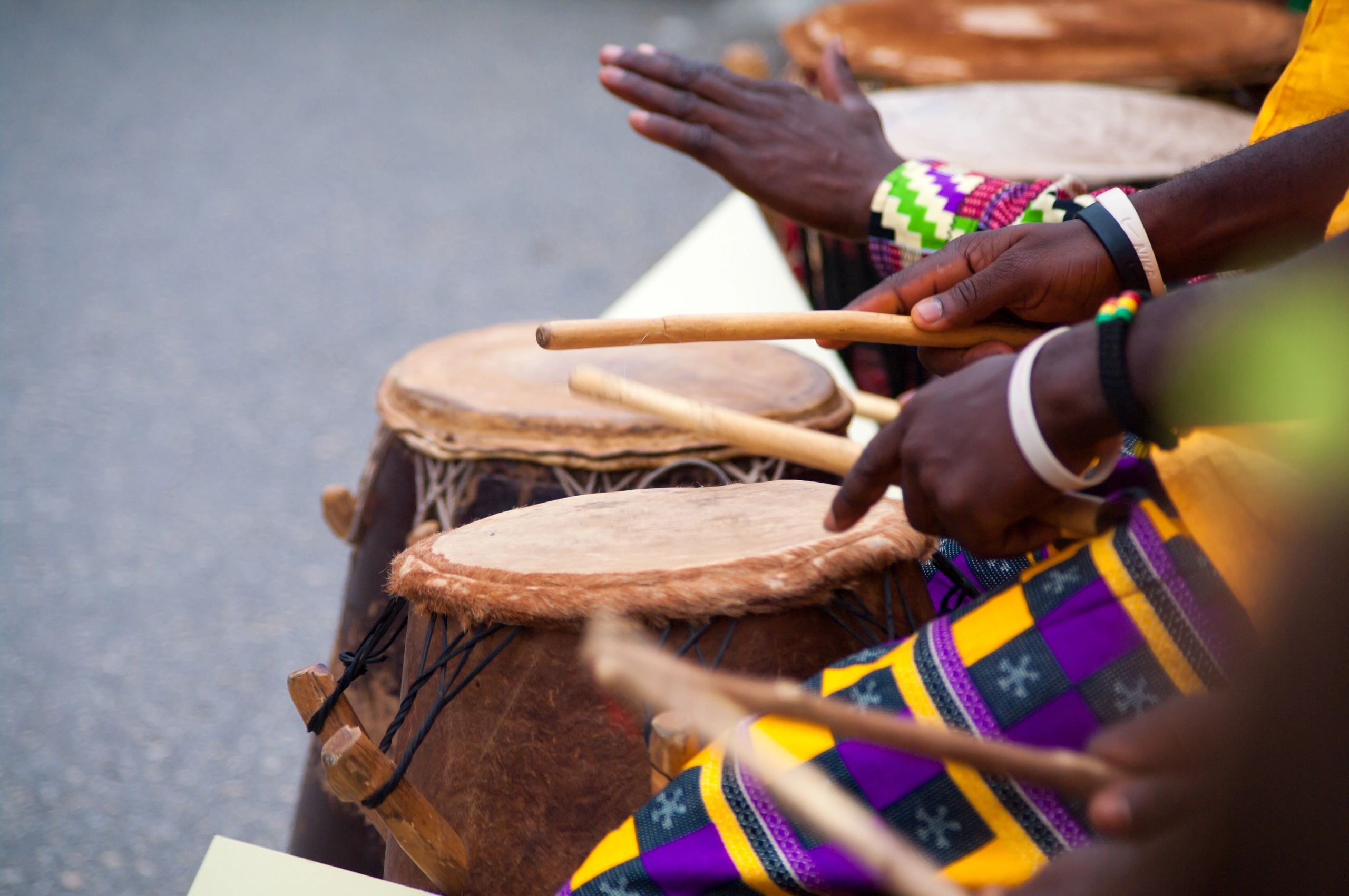 Close-up of hands playing traditional African drums with colorful attire.