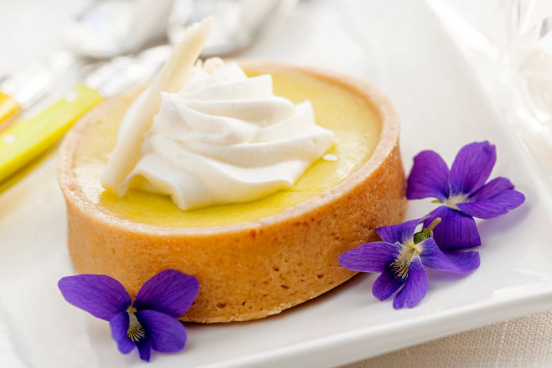 Fresh gourmet lemon dessert tart with edible violet flowers garnish