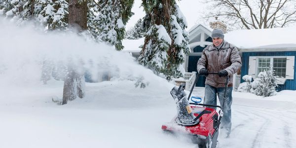 A truck equipped with a red snowplow clearing snow on a winter road.