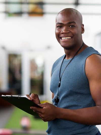 Smiling fitness trainer holding a clipboard in a gym.