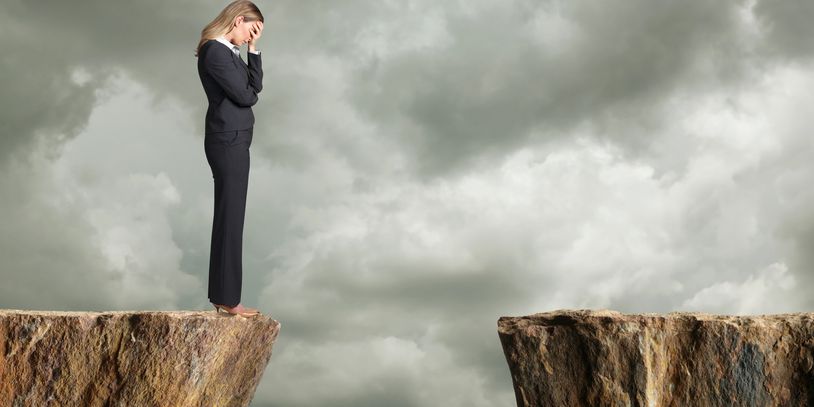 A worried woman stands on the edge of a cliff facing a large gap.