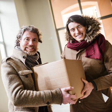 Two men smiling and holding a cardboard box indoors.