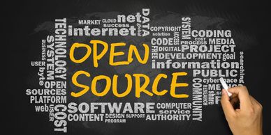 Hand writing 'Open Source' surrounded by related technology words on chalkboard.