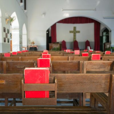Empty church pews with red hymnals and a cross at the altar.