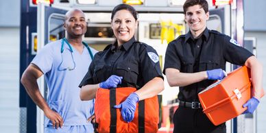 Three smiling emergency medical professionals standing in front of an ambulance.