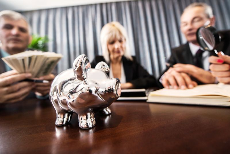 Business people having a meeting. Focus is on foreground, on a piggy bank.   