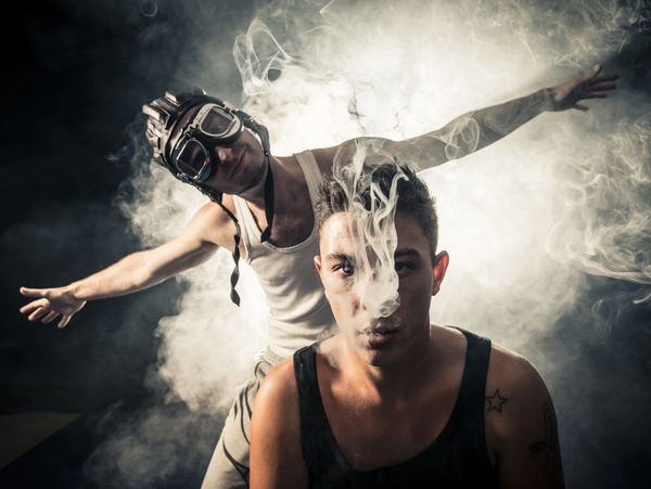Two young men surrounded by smoke, one blowing smoke towards the camera.