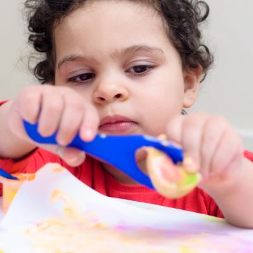 Young child focused on scooping food with a blue spoon.
