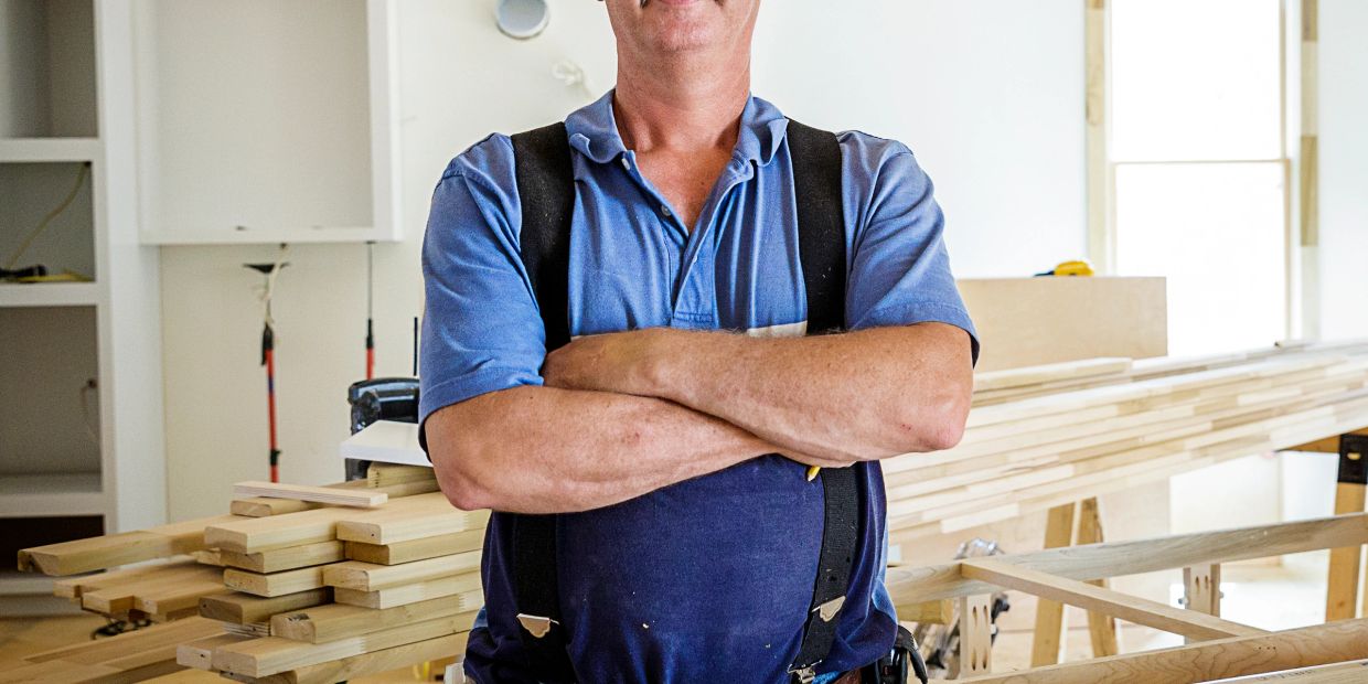 Carpenter standing with arms crossed in a woodworking shop.