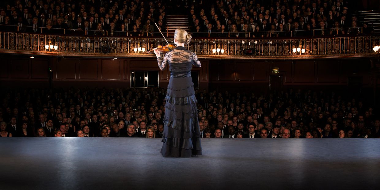 Violinist performing on stage to a large audience.