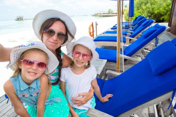 Woman and two girls in sunglasses and hats at a beach resort.