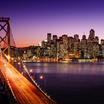 San Francisco skyline at dusk with illuminated Bay Bridge in foreground.
