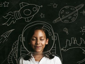Girl imagining space adventure with chalk-drawn astronaut helmet and planets.