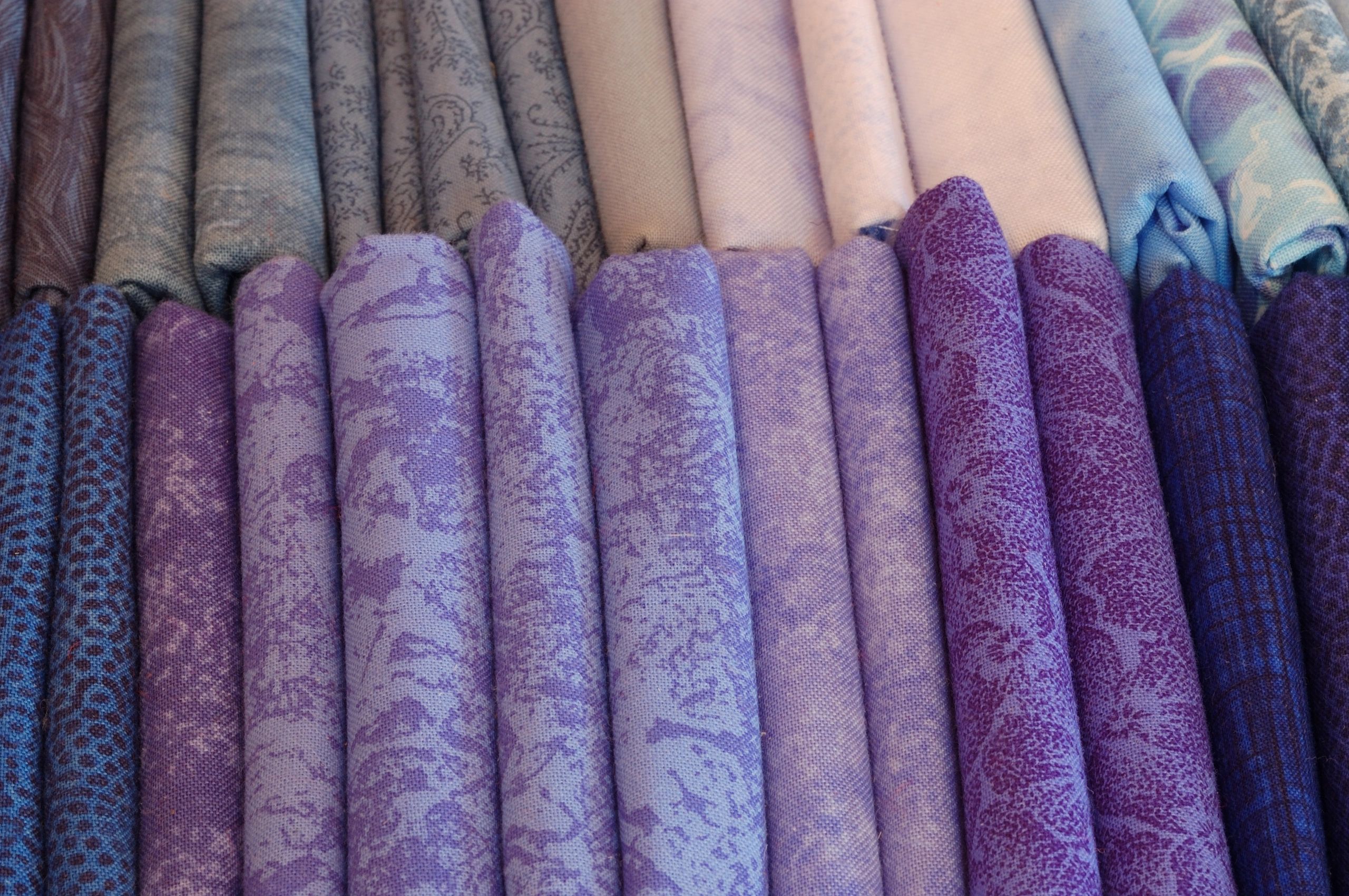 Rolls of fabric in various shades of blue and purple with different patterns.