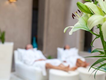 Close-up of white lilies with two people relaxing in the background.