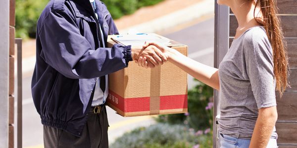 Delivery person shaking hands with woman after handing over a package.