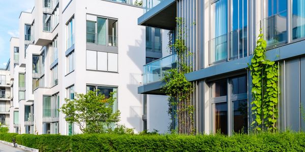Modern apartment buildings with greenery and large windows under clear sky.