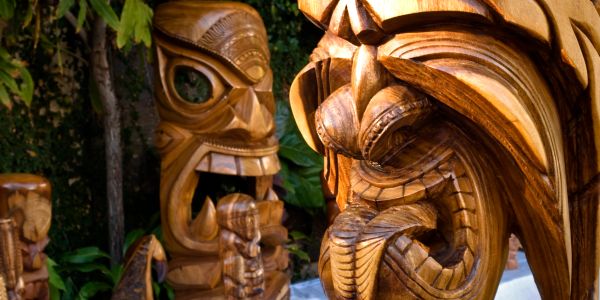 Intricately carved wooden tiki statues with fierce expressions in a lush outdoor setting.