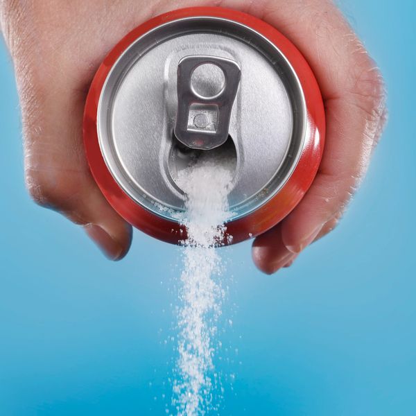 Hand pouring sugar from a red soda can against a blue background.