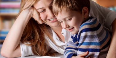 A mother and her son smiling together while reading.