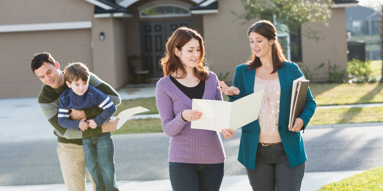 Real estate agent showing house plans to a couple outside their new home.