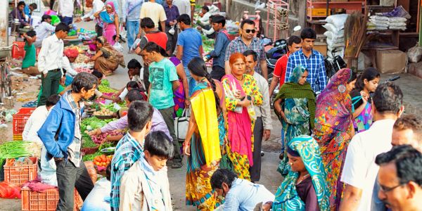 Busy outdoor market with people shopping and colorful vegetables.