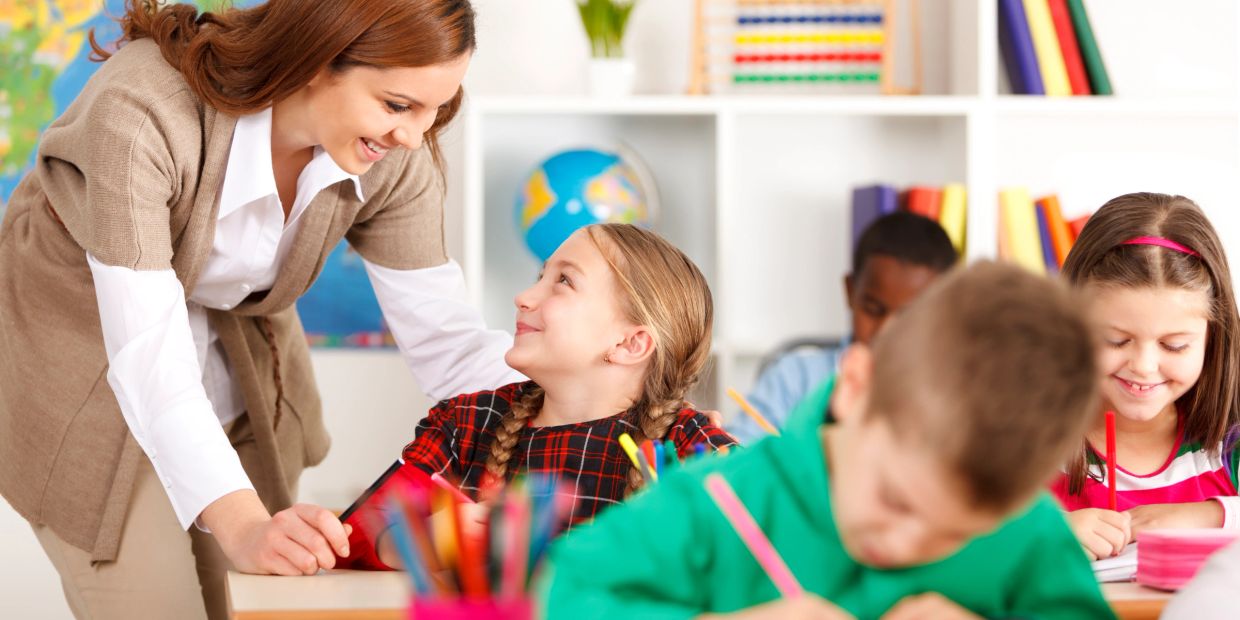 Teacher helping a smiling student in a classroom.