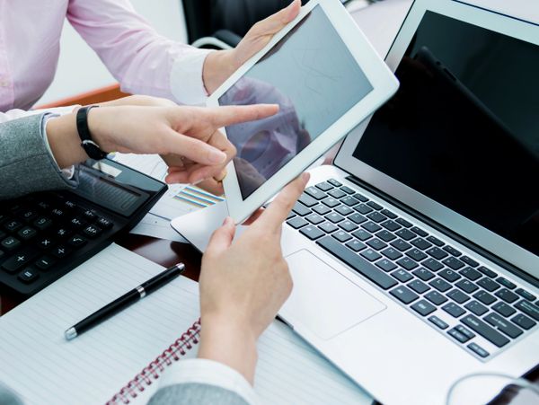 Two professionals discussing data on a tablet beside a laptop and calculator.