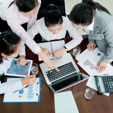 Four professionals collaborating around a laptop with charts and documents.