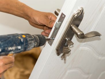 Person installing a door lock using a power drill.