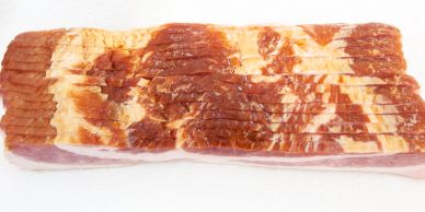 A slab of sliced uncooked bacon on a white surface.