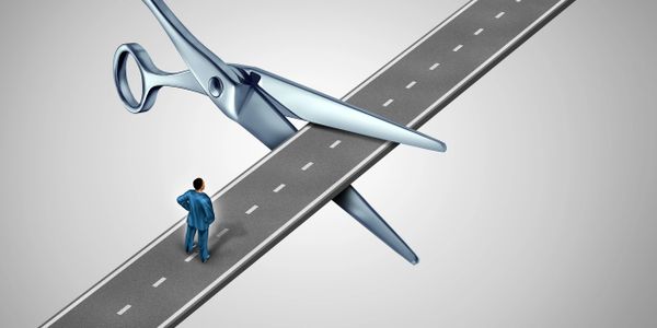 A man stands before giant scissors cutting a road, symbolizing a blocked path.