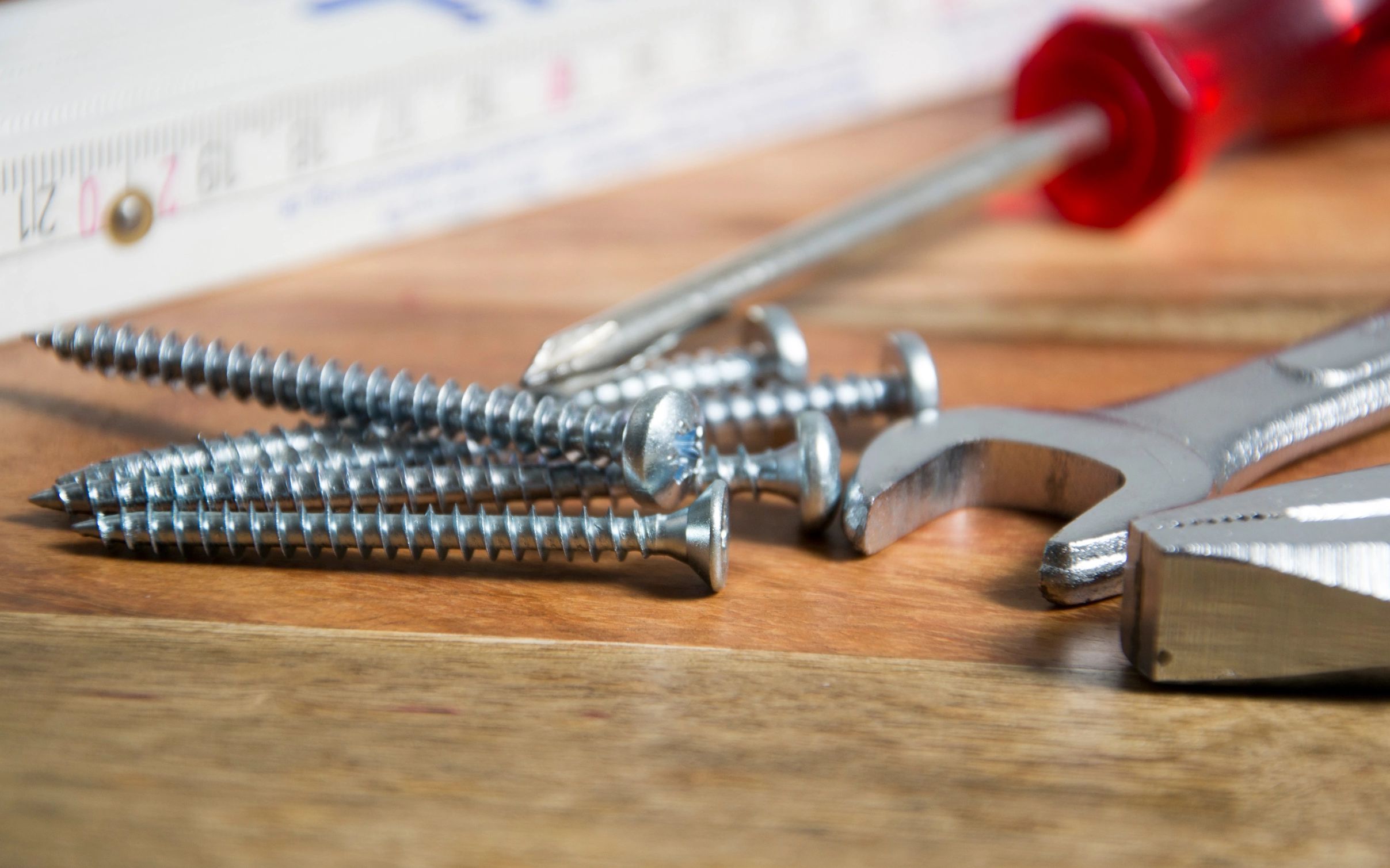 Close-up of screws and tools on a wooden surface.