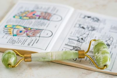 A green jade roller placed on an open anatomy book with colorful diagrams.
