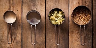 Four measuring cups with different dry ingredients on a wooden surface.